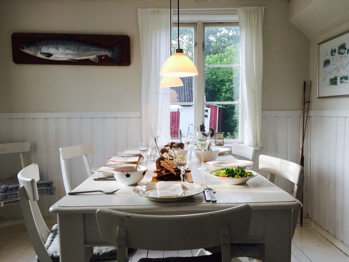 Dining room with a white wooden table set with plates, bowls, glasses and a hanging lamp above
