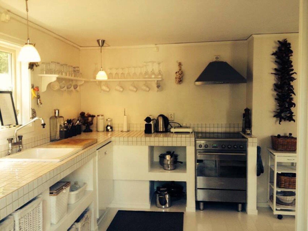 Kitchen with tiled counters, a sink, open shelving, hanging glasses and mugs, and a stainless steel oven