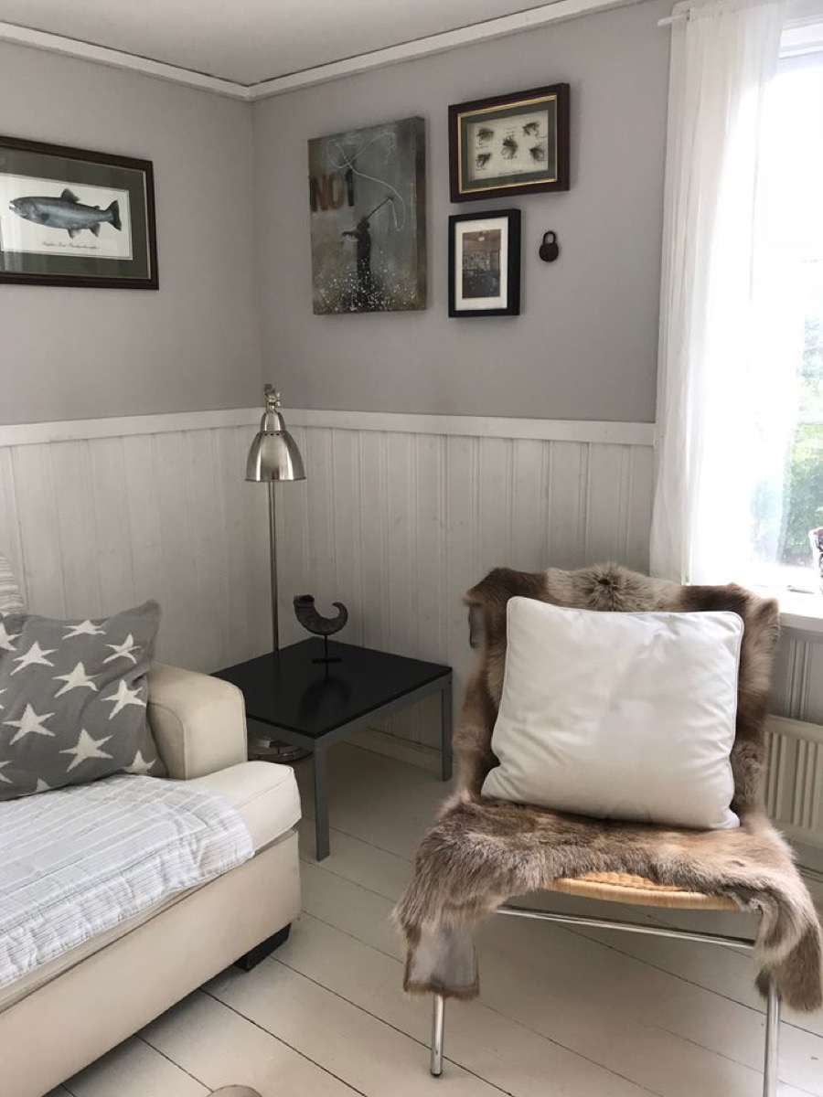 Living room corner with sofa, chair with fur throw and white cushion, small black table, and framed pictures on the wall