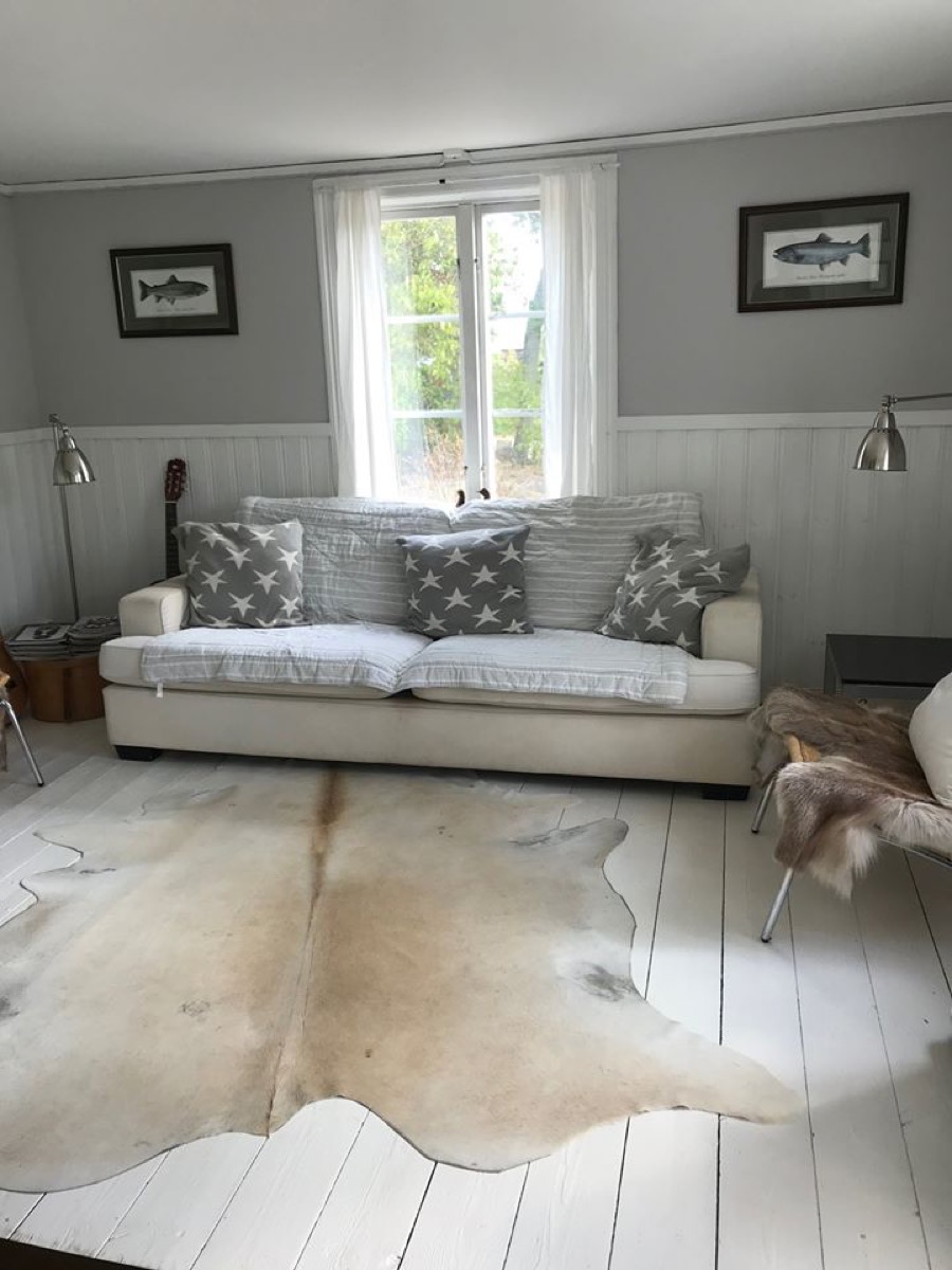 Living room with white sofa, cushions, animal skin rug on white floorboards, and a window